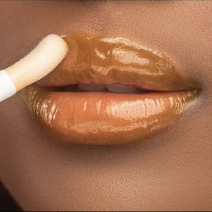 Lip model shot of golden Vanilla Sky Glow Lip Oil applied over medium-deep skin tone – radiant glass finish with hydrating glow.