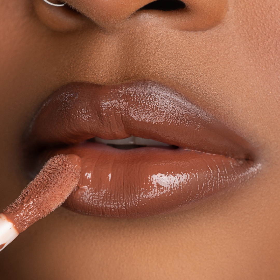 Lip-on model shot: Brown Suga Nude Glass Gloss applied on medium to deep skin tone — pigmented high-shine finish