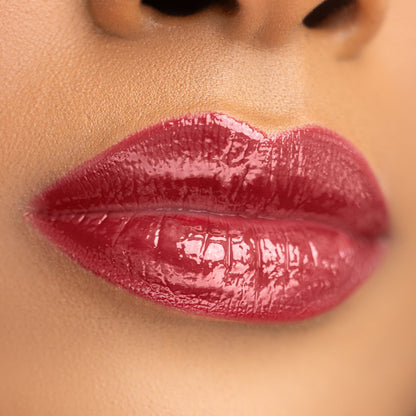 Swatch of Bold Lip Gloss shade ‘Burgundy’ on medium skin tone – deep wine red with mirror-shine finish