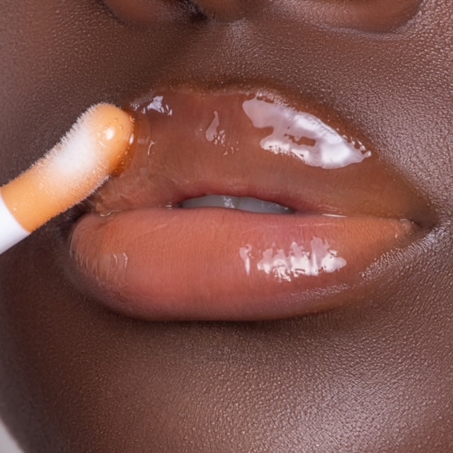 Lip model shot of orange SunGlow Glow Lip Oil applied over medium-deep skin tone – radiant glass finish with hydrating glow.