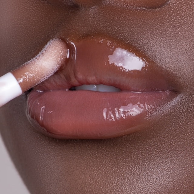 Lip model shot of brown SunKissed Glow Lip Oil applied over medium-deep skin tone – radiant glass finish with hydrating glow.