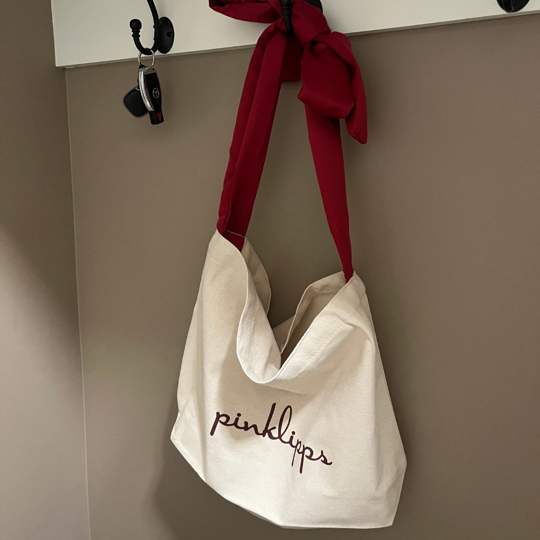 Pink Lipps Tote Bag detail shot showing burgundy logo emboss on tan canvas and burgundy strap knot detail